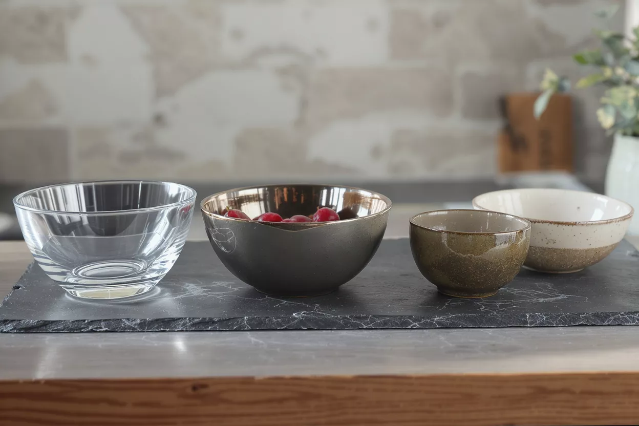 Four different bowls, including glass, ceramic, and speckled, on a slate board.