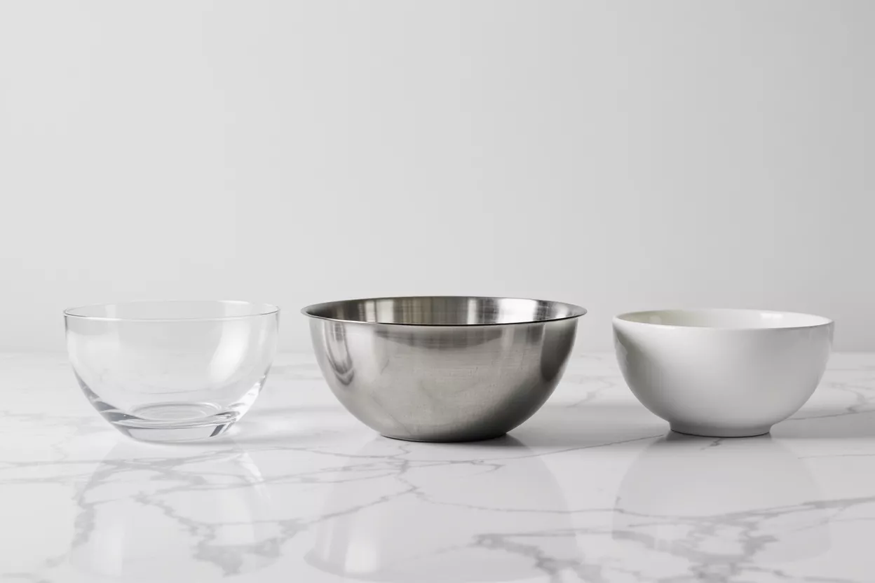 Three bowls: clear glass, stainless steel, and white ceramic on a marble surface.