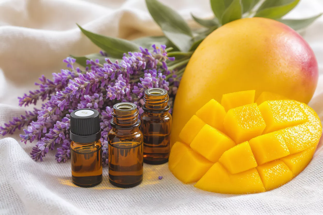 Three essential oil bottles with lavender and mango on a white cloth.