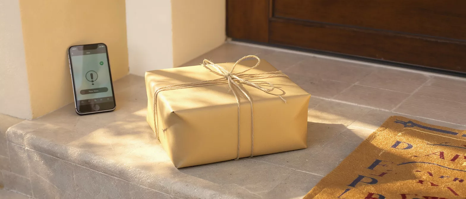 A package on a doorstep next to a phone displaying a delivery notification.