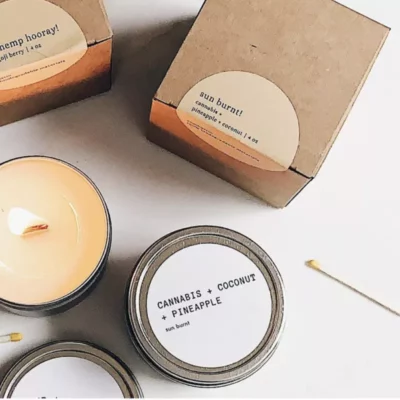 Scented hemp candles with coconut and pineapple aroma in metal tins and eco-friendly packaging.