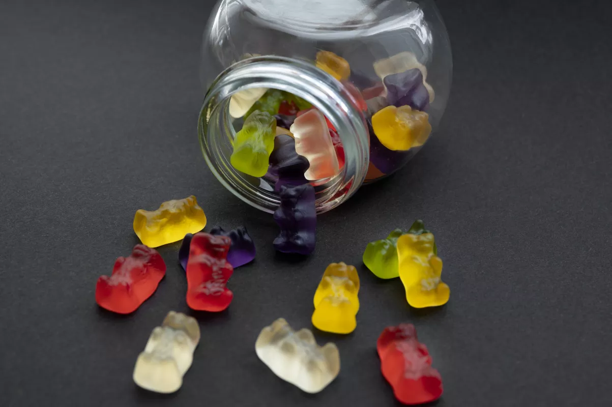 Colorful gummy bears spill from jar, showcasing vibrant, glossy treats on dark background.