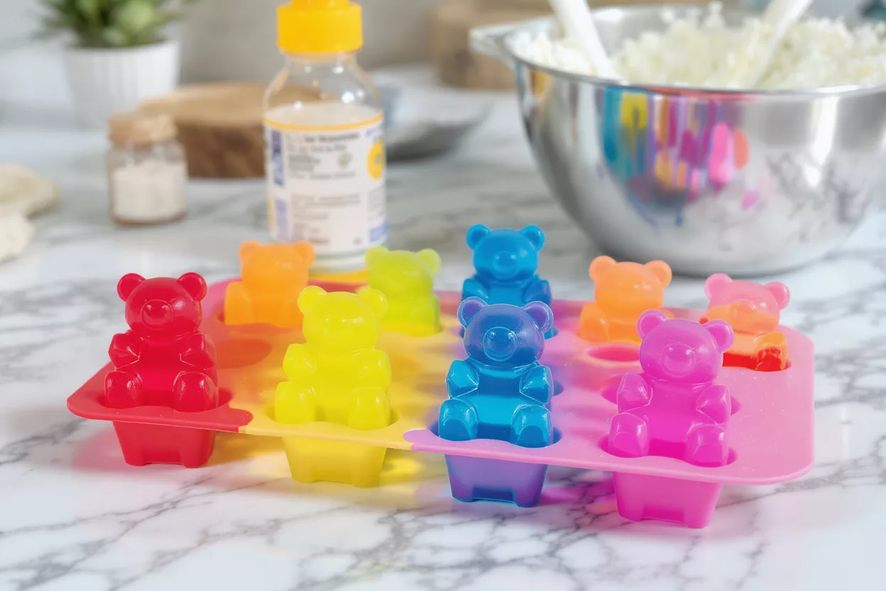 A silicone mold filled with colorful gummy bears on a marble countertop.
