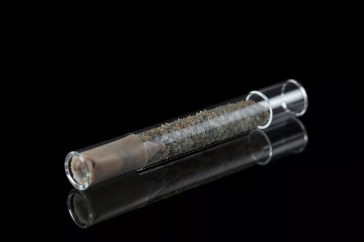 Clear glass tube containing light brown and gray granular material on black background.