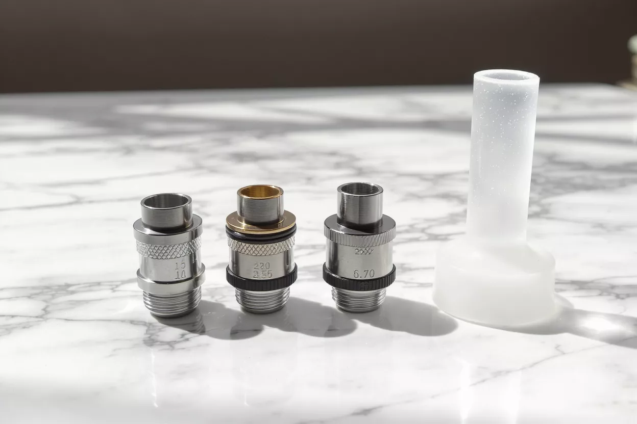 Three metal vape coils and a frosted glass mouthpiece on a marble surface.