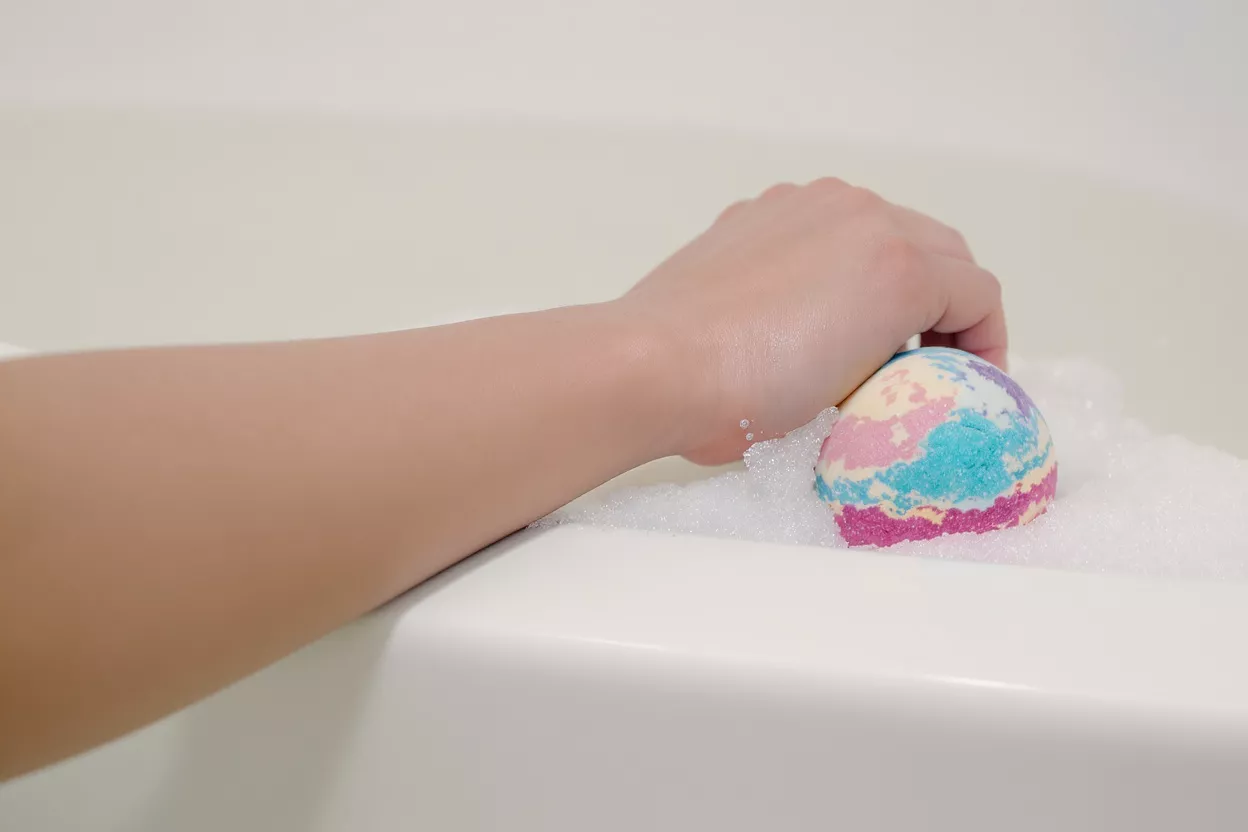 Bomba de baño colorida en la bañera Una mano colocando una bomba de baño vibrante y multicolor en una bañera blanca y burbujeante.