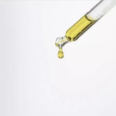 Golden CBD oil drop suspended from pipette against white background, highlighting viscosity and purity.