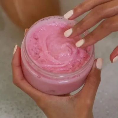 Close-up of hands holding open jar with pink Delush Whipped Soap Scrub for skincare.