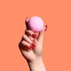 Hand holding pink bath bomb with orange background.