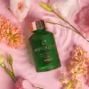 Luxurious sensual bath oil bottle with floral accents and elegant design on pink background.
