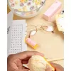 Breakfast scene with cereal bowl, reading glasses, word search, pastry, and orange being peeled.