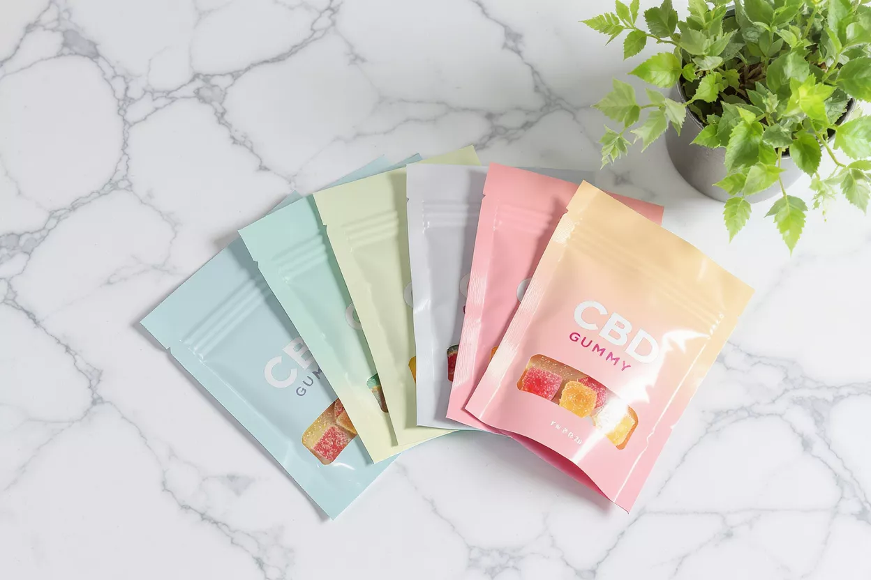 Colorful CBD Gummy Pouches A fan of colorful CBD gummy pouches with a plant on a marble surface.