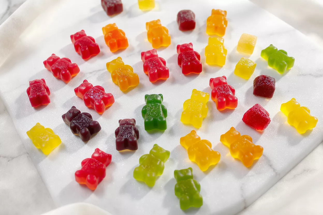 A variety of colorful gummy bears and cubes scattered on a white marble surface.