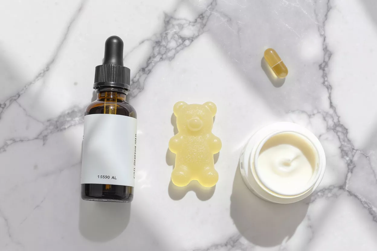CBD tincture bottle, coffee mug, and sleep mask on a bedside table.
