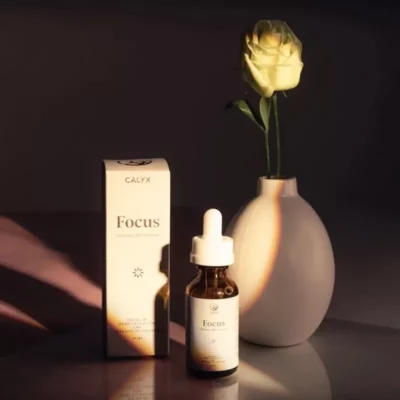 CALYX Focus CBD tincture with yellow rose on reflective surface for wellness.