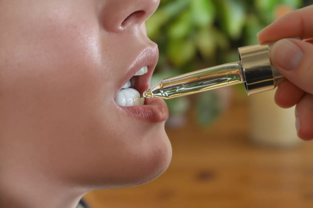 Close-up of a person taking liquid drops from a dropper into their mouth.