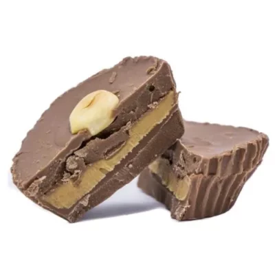 Halved white chocolate peanut butter cup with creamy filling and whole peanut on white background.