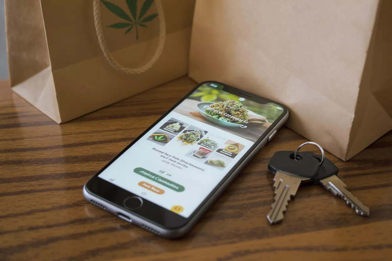 Smartphone displaying a cannabis delivery app next to keys and paper bags.