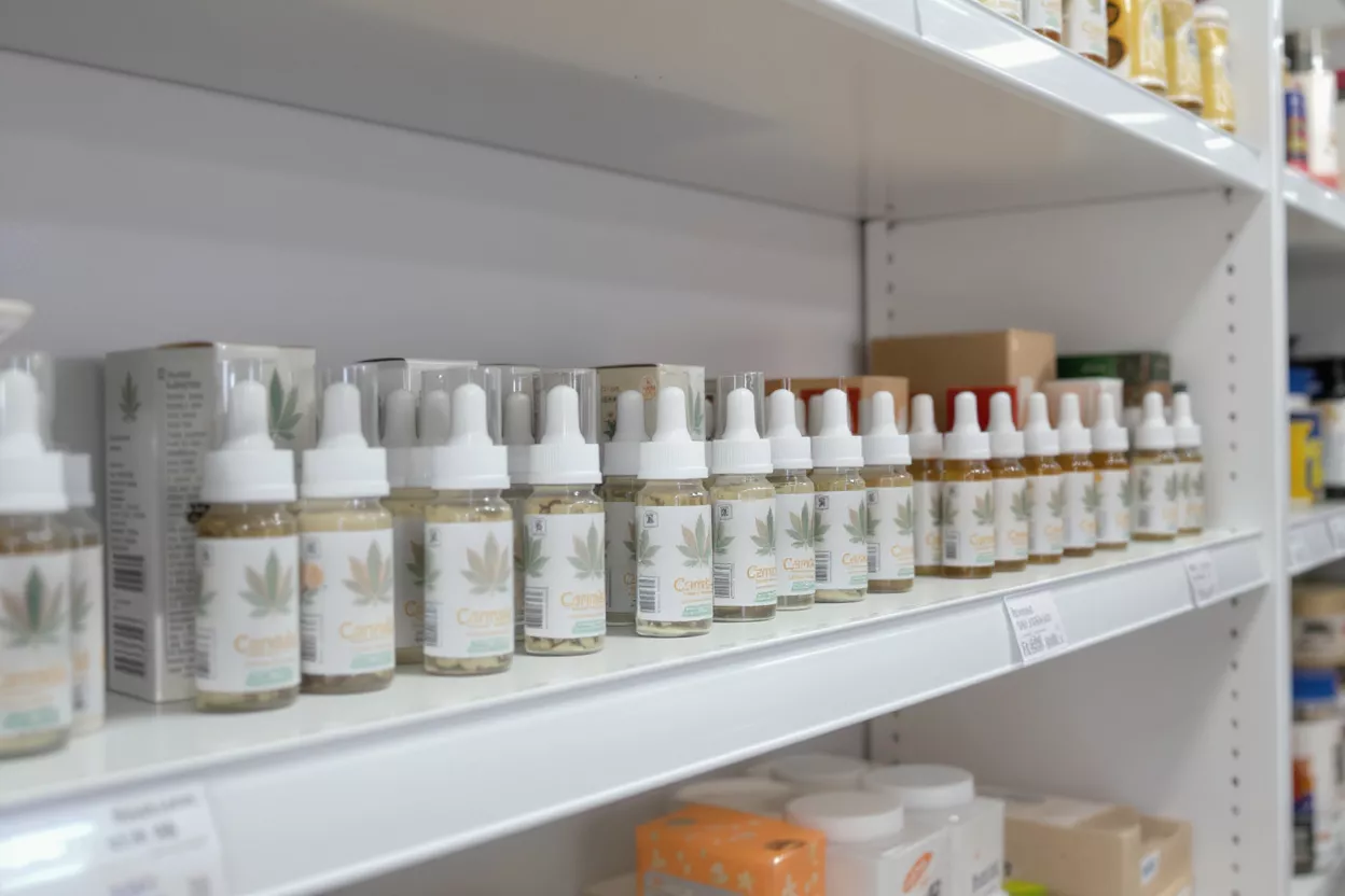 Numerous small bottles of CBD oil with droppers displayed neatly on a white shelf.