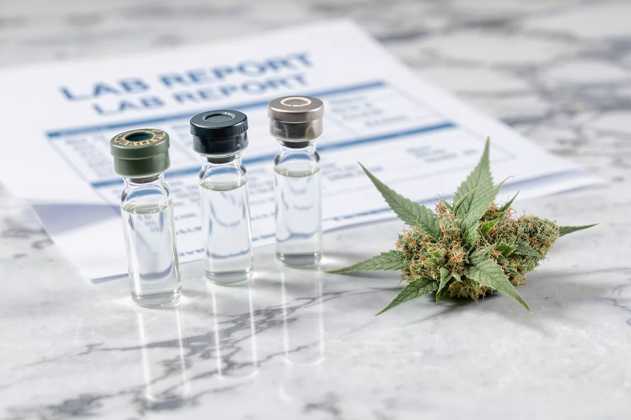 Three clear vials with liquid, cannabis bud, and lab report on marble surface.