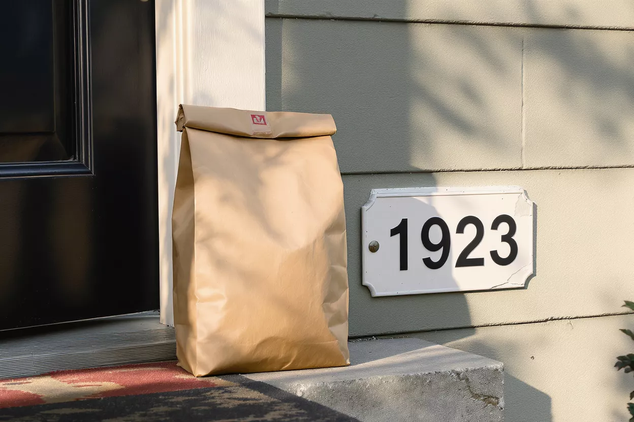Brown paper delivery bag on a doorstep next to an address sign.