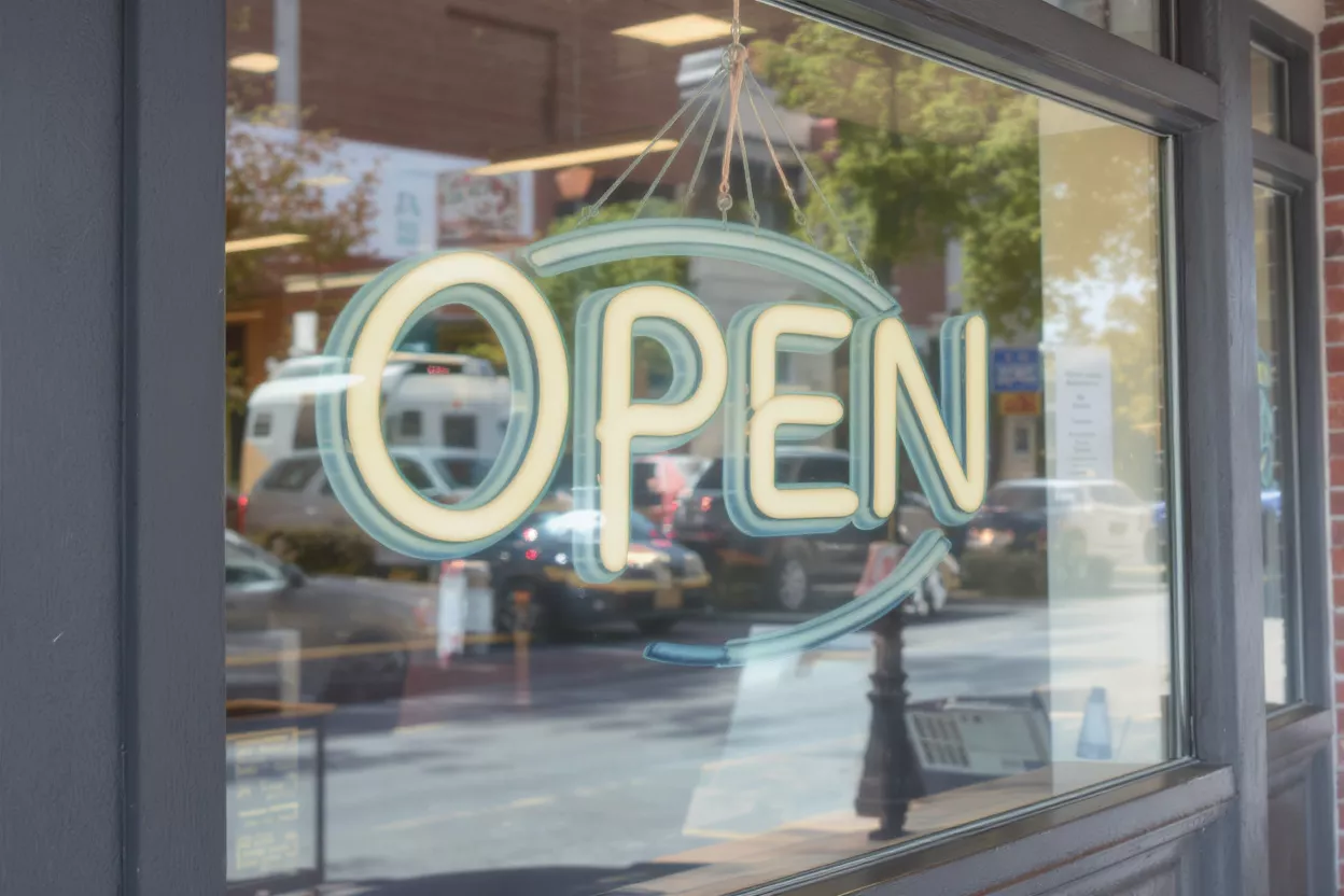 Neon Open Sign A neon 'OPEN' sign glows in a storefront window, reflecting street activity.