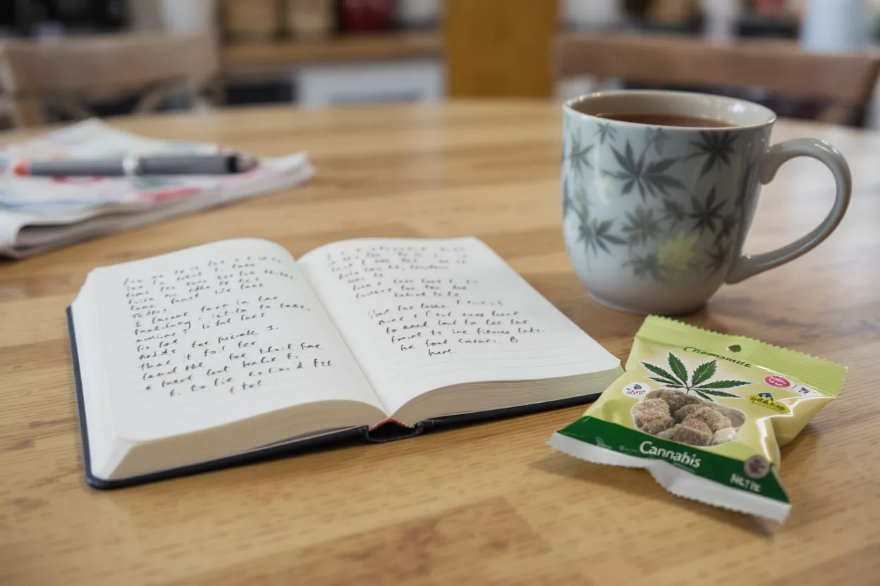 Cannabis-themed mug, journal, and chamomile cannabis edibles on a wooden table.