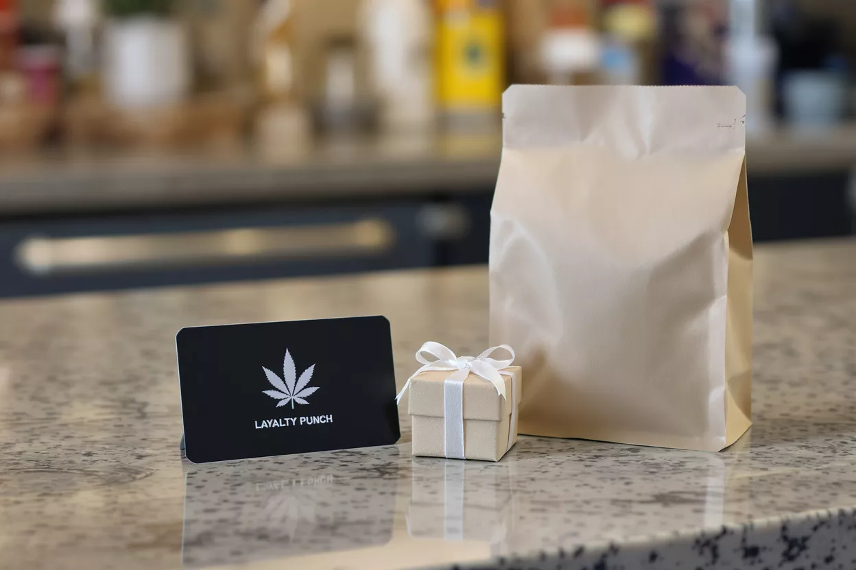 Cannabis Loyalty Program Black loyalty card, small gift box, and brown paper bag on a counter.