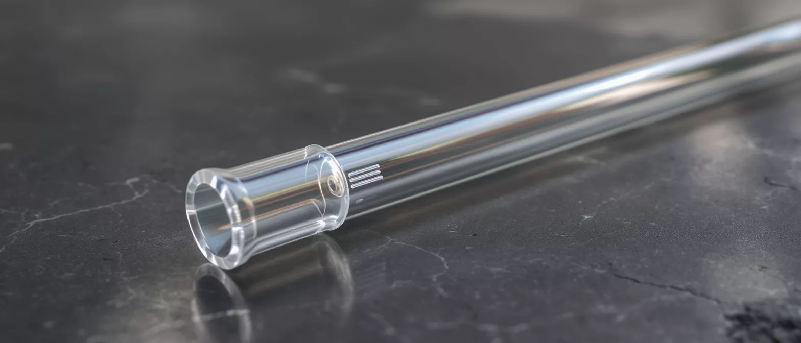 A clear glass tube with a flared end resting on a dark, textured surface.