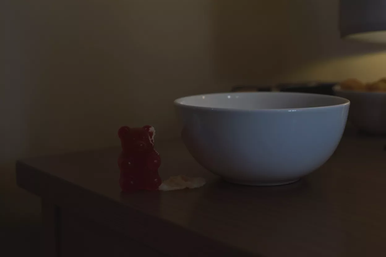 Red gummy bear beside a white bowl on a table