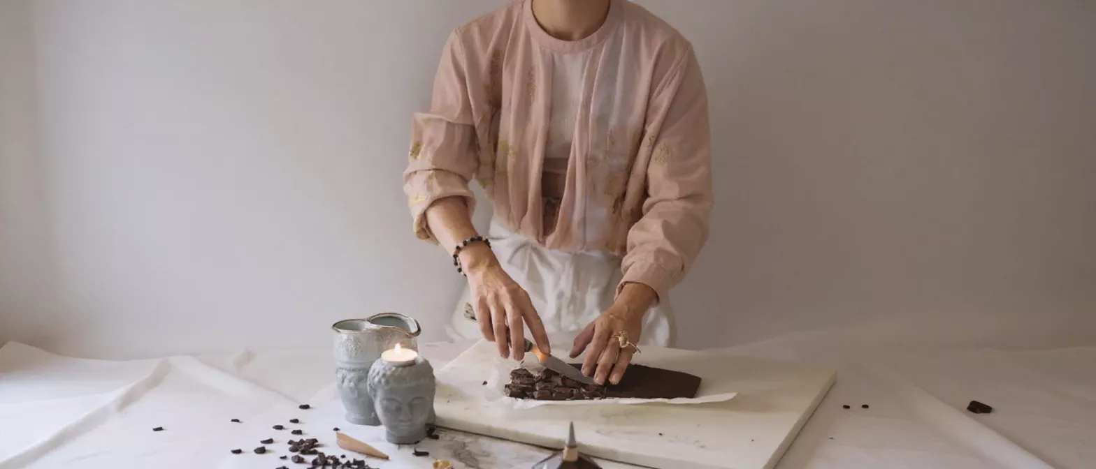 Person in pink shirt cutting a large chocolate bar on a white surface.