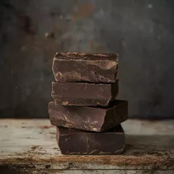 Stacked dark chocolate blocks on a rustic wooden table with a textured, artisanal feel.