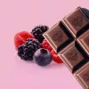 Chocolate bar with heart design and fresh berries on pastel pink background.