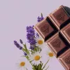 Chocolate bar with heart squares, lavender sprigs, and daisies on a purple background.
