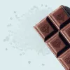 Artisanal dark chocolate bar with heart emblems, featuring coarse salt on a blue background.