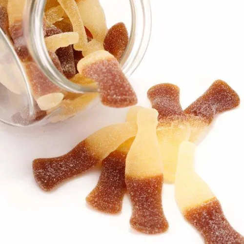 Haribo fizzy cola bottle gummies spill from jar on white background.
