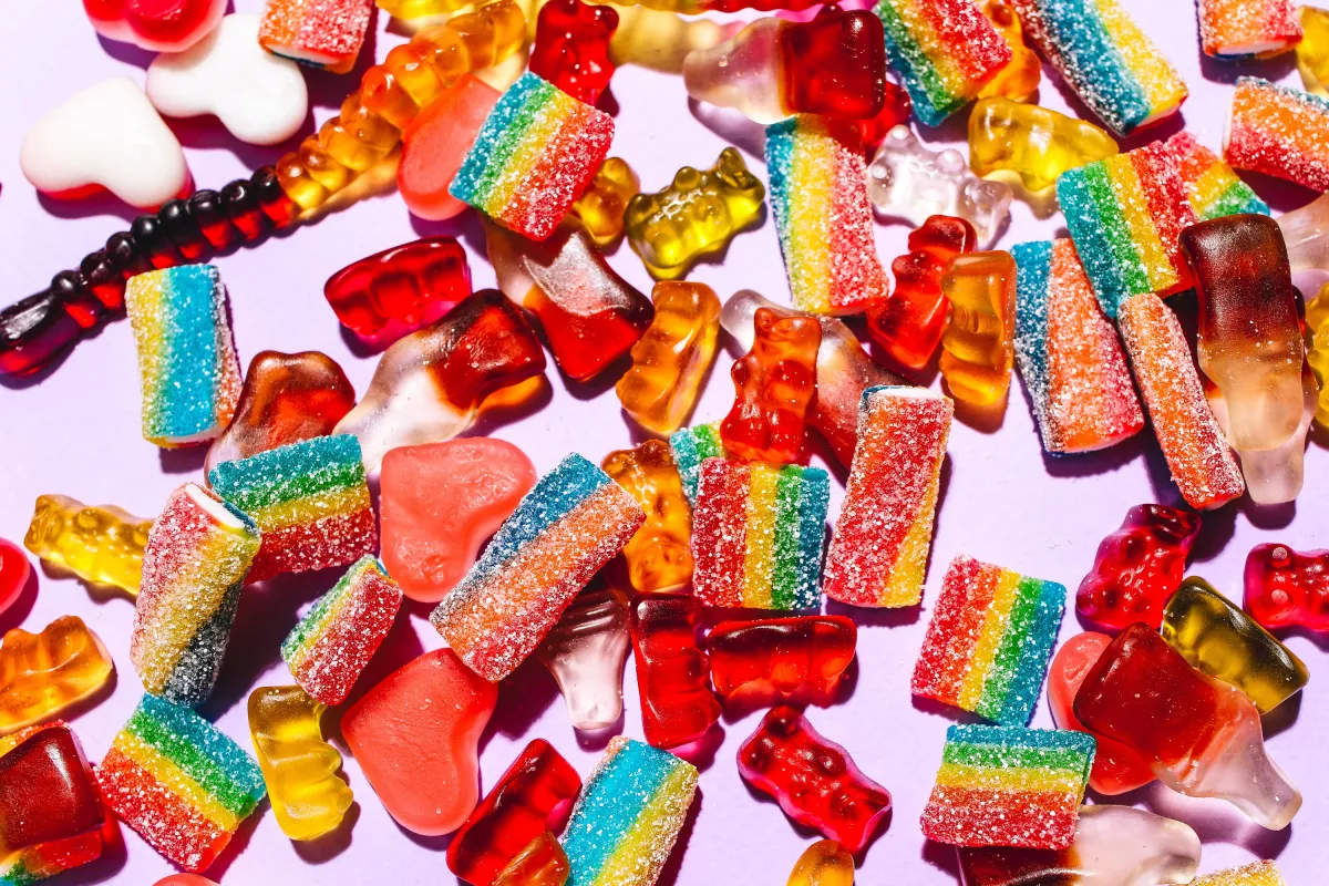 Colorful gummy candy assortment with bears, hearts, and jelly strips on pink background.