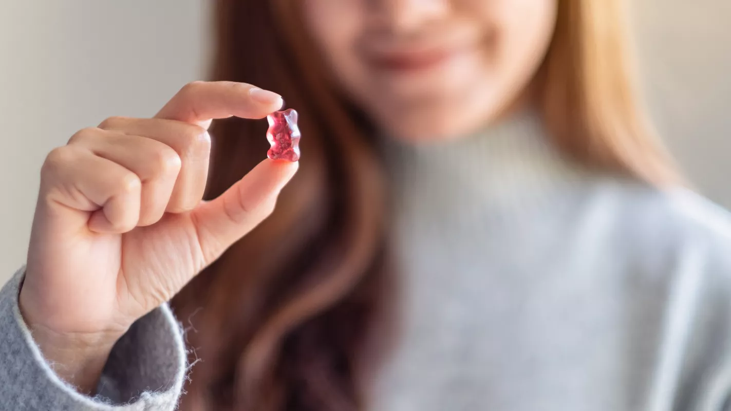 Person smiling while holding a juicy red gummy bear candy, perfect for a sweet snack.