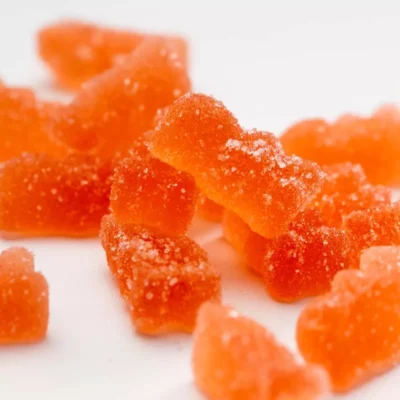 Close-up of orange KK Indica Bears gummy candies with sparkling sugar coating.