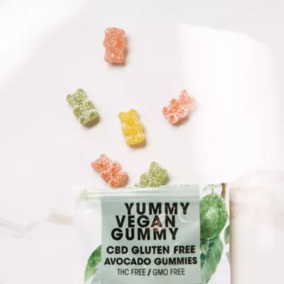 Colorful vegan CBD gummy bears, gluten-free, THC-free, GMO-free, displayed with avocado-leaf packaging.