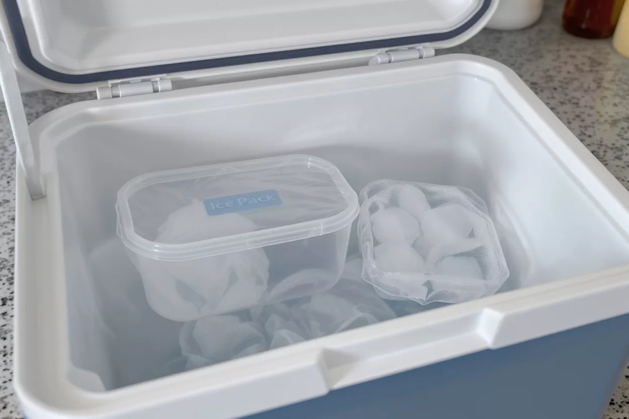 An open white and blue cooler containing an ice pack and a mesh bag of ice.