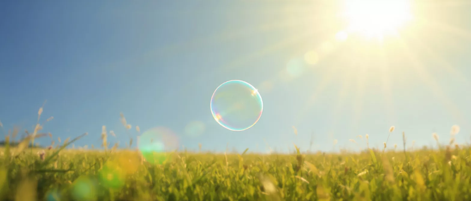 A bubble floating above green grass under a clear sky