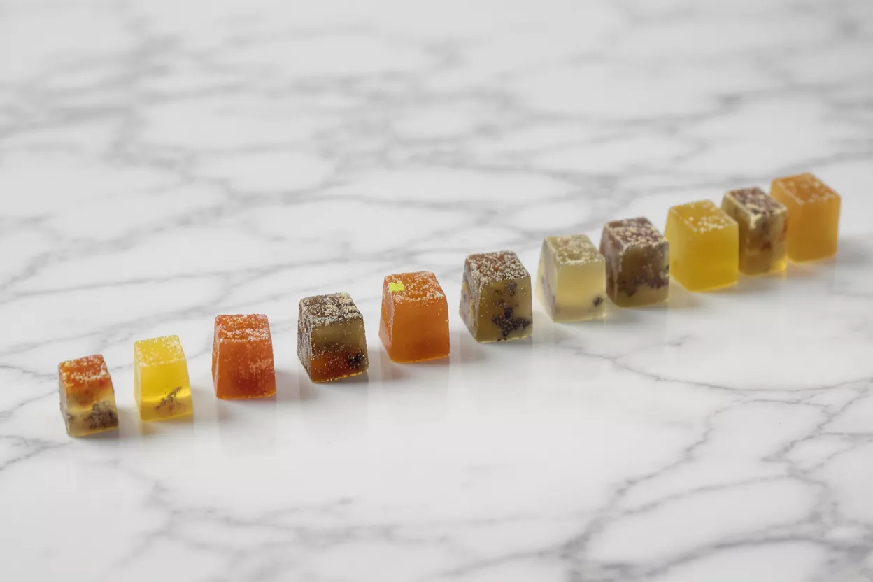 A row of colorful, square gummies on a white marble surface.