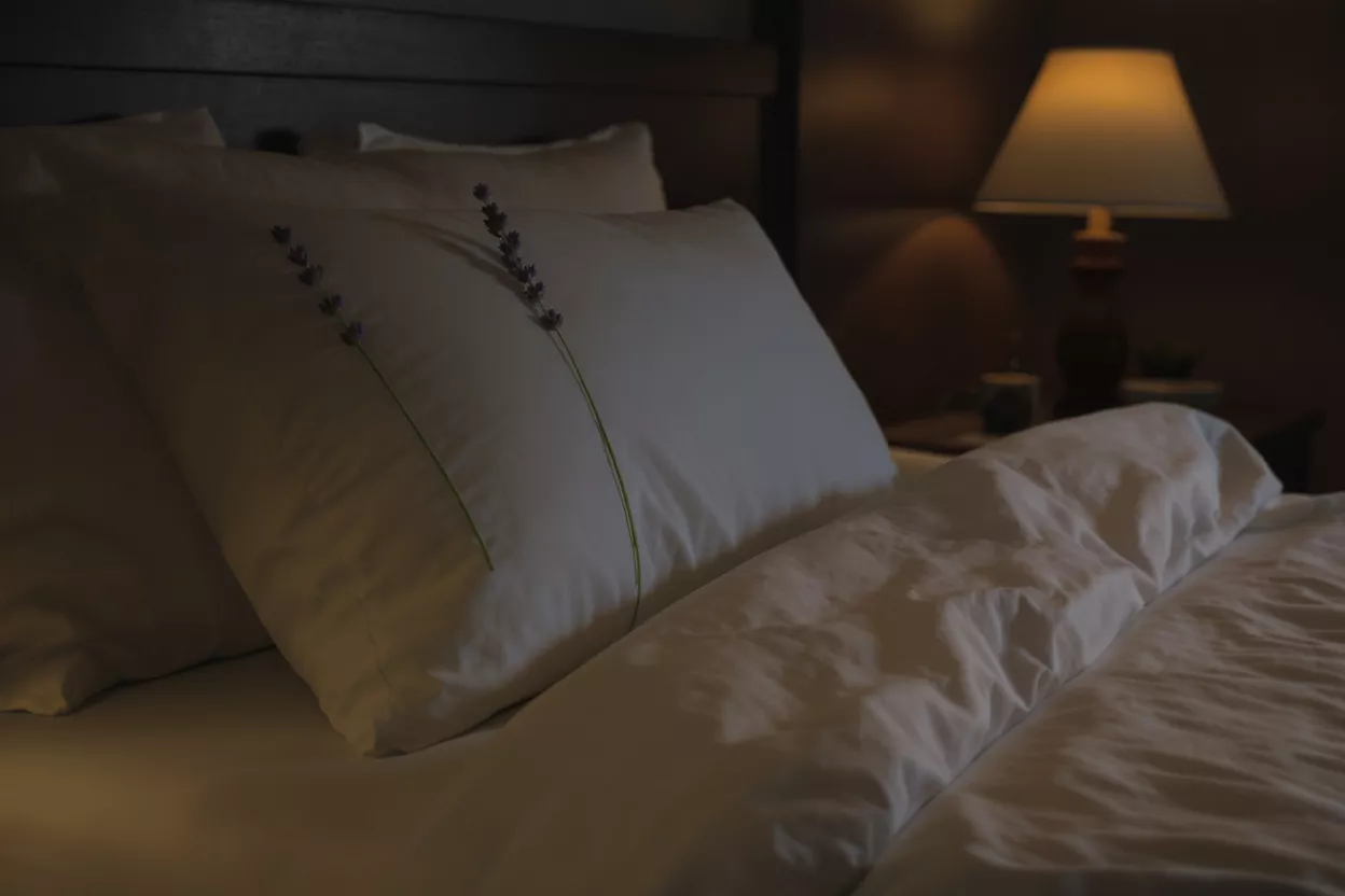 A cozy bed with white pillows and duvet, adorned with lavender sprigs.