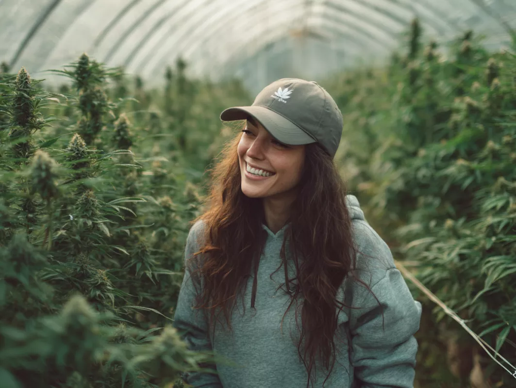 Young woman joyfully stands in vibrant cannabis greenhouse with lush, thriving plants.