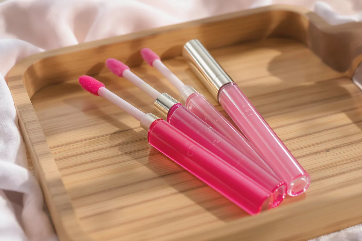 Pink Lip Gloss Collection Four tubes of pink lip gloss on a wooden tray