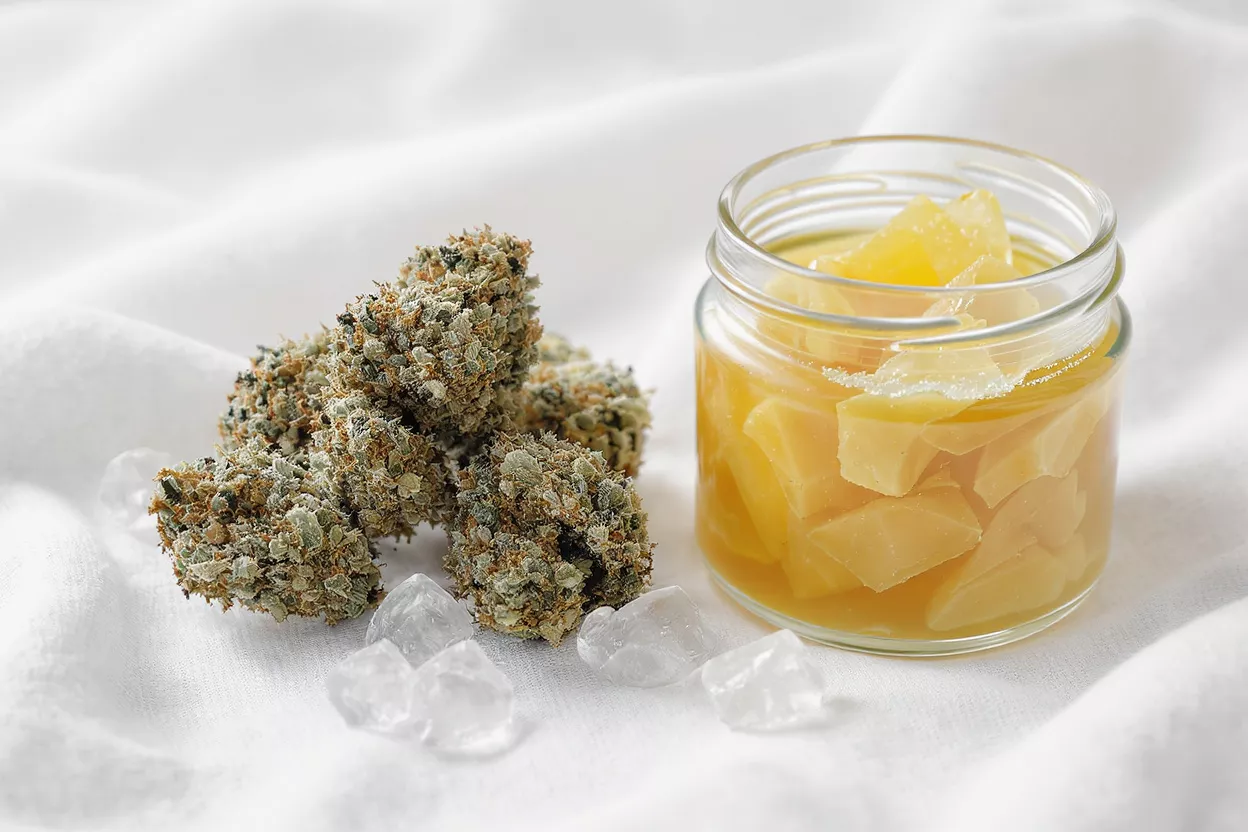 Trichome-covered cannabis buds sit beside a jar of yellow concentrate and loose THC diamonds.