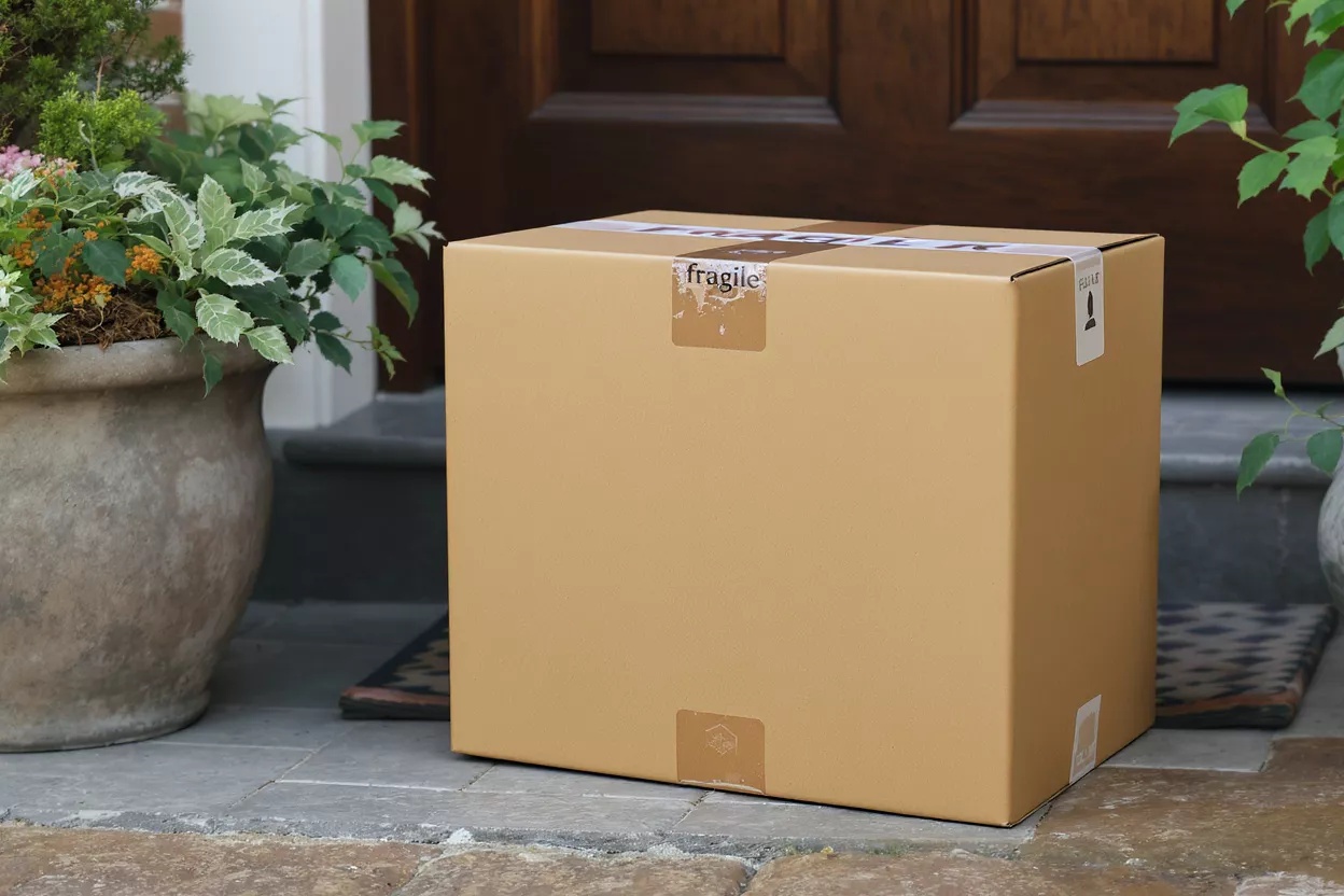 A brown cardboard box with 'fragile' stickers sits on a doorstep.