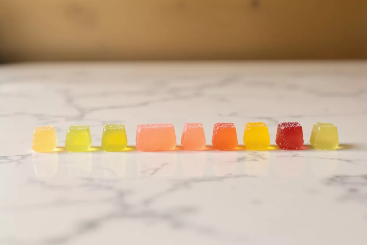 Nine colorful gummy candies in a row on a white marble surface.