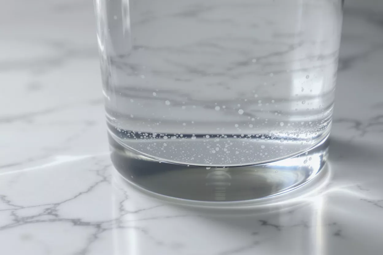 Close-up of a glass of sparkling water with bubbles on a white marble surface.